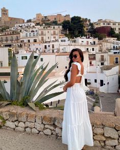 a woman standing on top of a stone wall next to a large plant and buildings