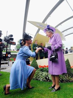 two women in purple dresses and hats are shaking hands with each other on the grass