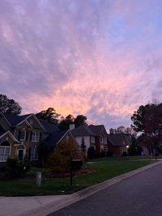 a street lined with houses under a cloudy sky at dusk in the suburbs, as seen from across the street