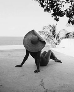 a woman laying on the ground with a hat on her head looking out at the ocean