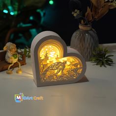 an illuminated heart shaped box on top of a table with flowers and other decorations in the background