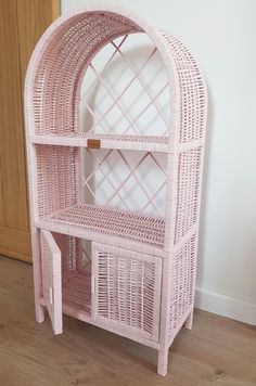 a pink wicker shelf with a mirror on it's top and shelves below