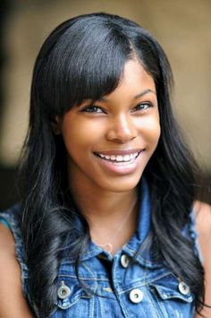 a woman with long black hair smiling at the camera and wearing a denim shirt over her shoulders