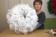 a woman is holding up a wreath made out of plastic cups and yarns on a table