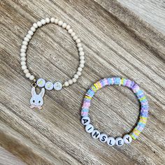 two bracelets with name charms on them sitting on top of a wooden table next to each other