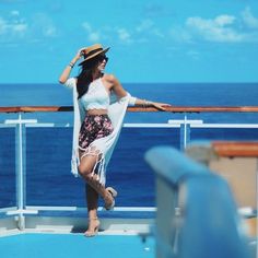 a woman standing on the deck of a boat in front of the ocean wearing a hat