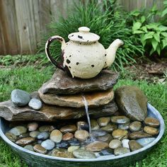 a tea pot is sitting on top of some rocks in the grass and water coming out of it