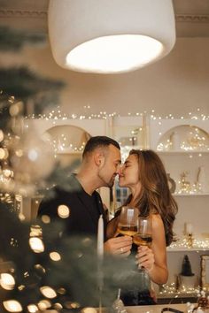 a man and woman sharing a kiss in front of a christmas tree with wine glasses