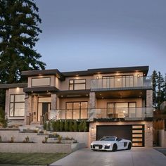 a white car parked in front of a large house at night with lights on the windows