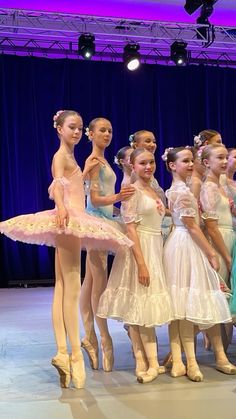 a group of young ballerinas standing next to each other in front of a stage