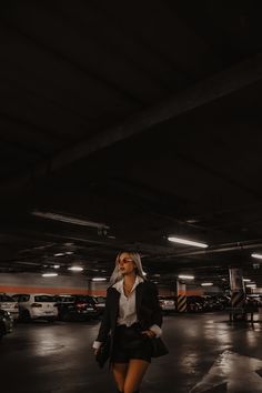 a woman in a white shirt and black skirt walking through a parking garage with her hand on her hip