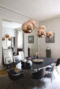 a dining room table with chairs and lights hanging from it's ceiling, in front of pictures on the wall