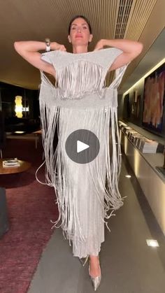 a woman in a white fringe dress walking down a hallway with her hands on her hips