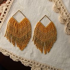 These maxi fringe earrings include three beautiful tones of premium Japanese Miyuki glass beads combined with small gold round beads to create an elegant V pattern. The beads are hand strung and hang from a gold filled square finding.  The have fantastic movement and just the right the amount of sparkle. The square finding is hung from a hypoallergenic 14K gold plated ear wire. These earrings are designed by myself and made in conjunction with my team of women artisans from vulnerable communitie Bohemian Gold Rectangular Beaded Earrings, Bohemian Gold Tassel Earrings With Round Beads, Gold Bohemian Beaded Earrings With Faceted Beads, Gold Bohemian Tassel Earrings, Gold Fringe Beaded Dangle Earrings, Gold Beaded Fringe Dangle Earrings, Gold Beaded Dangle Earrings With Tassels, Gold Tassel Earrings With Beaded Fringe, Gold Beaded Earrings With Fringe