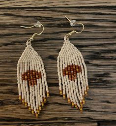 white and brown beaded earrings with wooden beads hanging from hooks on a wooden surface