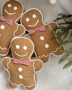 four decorated gingerbread cookies sitting on top of a white surface next to a christmas tree