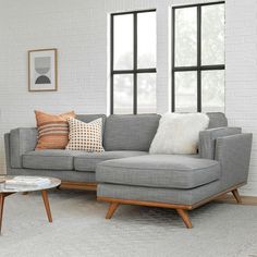 a living room with grey couches and pillows on the floor next to two windows