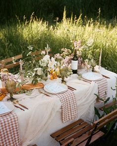 a table set up with place settings and flowers on it for an outdoor dinner party