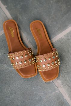 Effortlessly elevate your summer style with the Mindee Studded Sandal. Crafted from a sleek faux leather material, this sandal features a chic tan top strap adorned with gold studded accents. The flat design offers comfort and versatility, perfect for any warm weather occasion. Step out in style and confidence with these trendy sandals. Run true to size! Gold Studded Open Toe Sandals, Gold Studded Sandals For Summer, Leather Sandals With Gold Studs For Summer, Summer Gold Sandals With Gold Studs, Leather Sandals With Gold Studs For Spring, Casual Sandals With Gold Studs For Summer, Casual Gold-studded Sandals For Summer, Summer Beach Sandals With Gold Studs, Trendy Gold-studded Open Toe Sandals