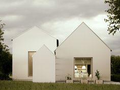 two white houses sitting next to each other on top of a grass covered field with trees in the background