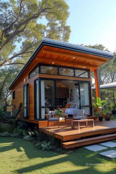 a small house with wooden decking in the grass next to some trees and plants