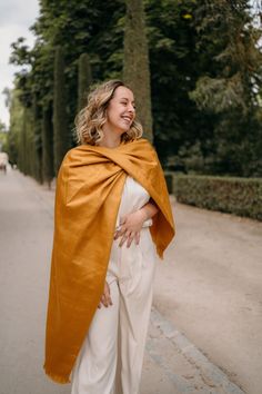 a woman in white pants and a yellow shawl smiles as she walks down the street