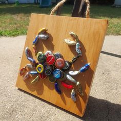 a wooden sign with several different colored bottle caps attached to it's sides and hanging on a rope