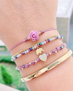 three different bracelets with charms and flowers on the wrist, one has an elephant charm