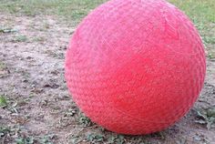 a large red ball sitting in the middle of a grass and dirt covered field,