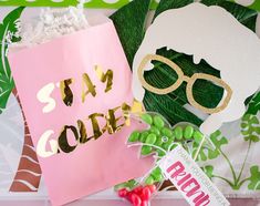 a pink paper bag with gold foil lettering on it next to some green and white decorations