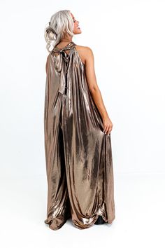 - Make a bold style statement with this glam jumpsuit! - Sleek, metallic, gold colored material - A built-in lining that ends thigh length - A mock neckline with back tie closure with a keyhole detail - Low back zip closure - A sleeveless cut - An ultra-relaxed silhouette that ends in wide floor length hemlines Chic Metallic Jumpsuits And Rompers For Party, Chic Gold Jumpsuits And Rompers For Night Out, Gold Jumpsuits And Rompers For Summer Evenings, Gold Jumpsuits And Rompers For Summer Party, Gold Evening Jumpsuits And Rompers For Summer, Gold Jumpsuit And Romper For Summer Party, Gold Chic Jumpsuit For Night Out, Chic Gold Jumpsuit For Night Out, Elegant Gold Jumpsuits And Rompers For Summer