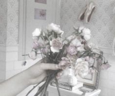 a person holding flowers in their hand near a mirror with shoes on the wall behind them