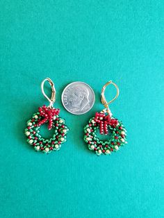 two beaded christmas wreaths are next to a penny on a green surface,