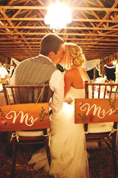 a bride and groom kissing in front of a wooden mr and mrs sign at their wedding reception