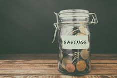 a glass jar filled with coins sitting on top of a wooden table next to a sign that says savings