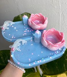 a hand holding a blue tray with two pink flowers on it and pearls around the edges