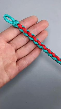 a hand holding a blue and red rope on top of a gray surface with one end twisted up