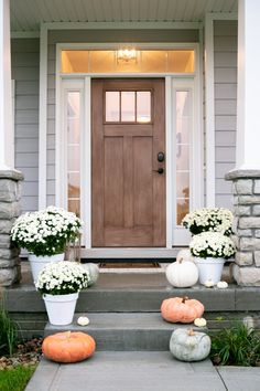 two white pumpkins sitting on the steps in front of a gray house with flowers