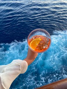 a person is holding up a glass with an orange slice in it on a boat