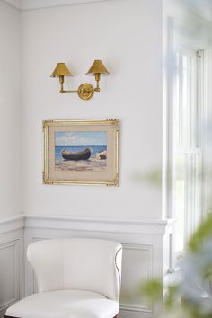 a white chair sitting in front of a painting on the wall next to a lamp