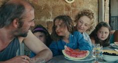 a group of people sitting at a table with watermelon slices on the plate