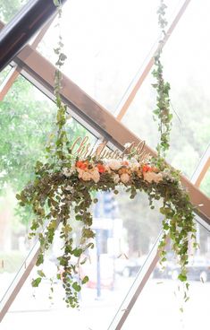 an arrangement of flowers and greenery hangs from the ceiling in front of a window