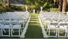 an outdoor ceremony setup with white chairs and flowers on the grass in front of palm trees