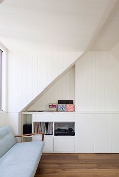 a white couch sitting under a window next to a shelf filled with books and records