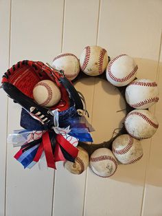 a wreath made out of baseballs and mitts is hanging on the wall with ribbon