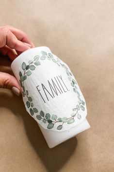 a person is holding a coffee cup with the word family on it and green leaves