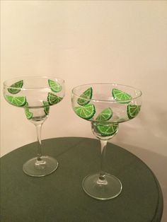 two wine glasses with lime slices in them sitting on a table next to each other