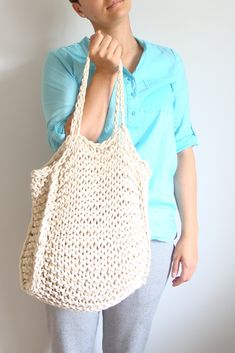 a woman is holding a crocheted bag in front of her face and looking at the camera