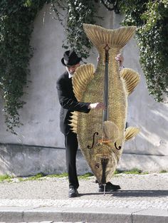 a man in a black suit and hat is holding a large fish costume on the street