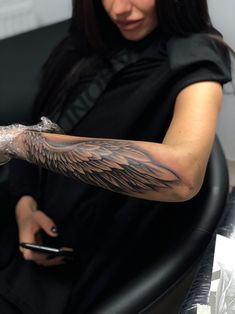 a woman getting her arm tattooed with an angel wing tattoo